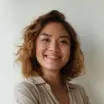 Customer portrait featuring a cheerful young woman with curly hair and a warm smile, dressed in a beige outfit, who appears pleased with her experience using our cryptocurrency exchange services.